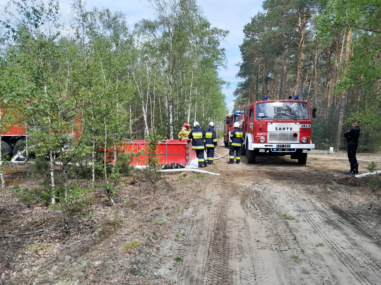 Samochód strażacki po prawo, po lewo zbiornik strażacki na wodę w tle las