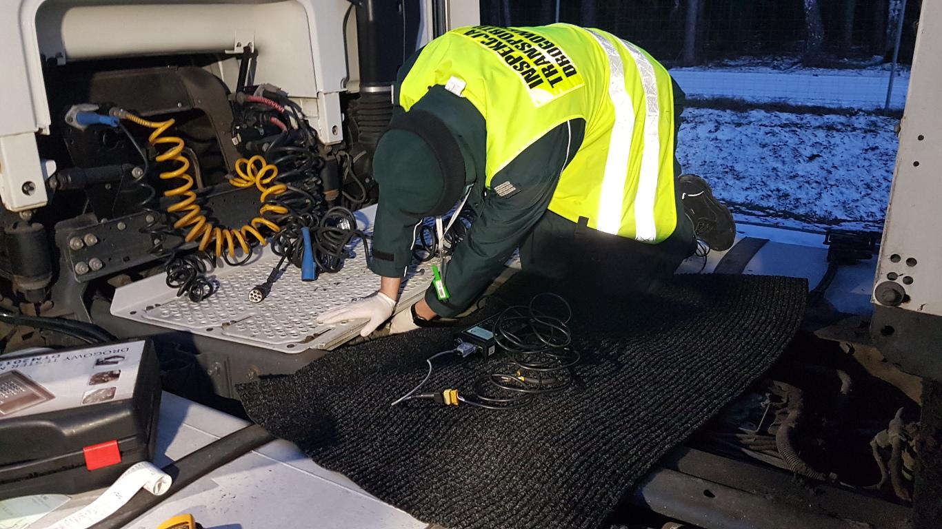 Inspektor transportu drogowego kontroluje instalację tachografu ciężarówki.