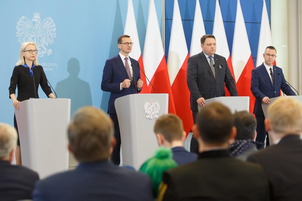 Premier Mateusz Morawiecki oraz inny mówcy stoją przy mównicach.