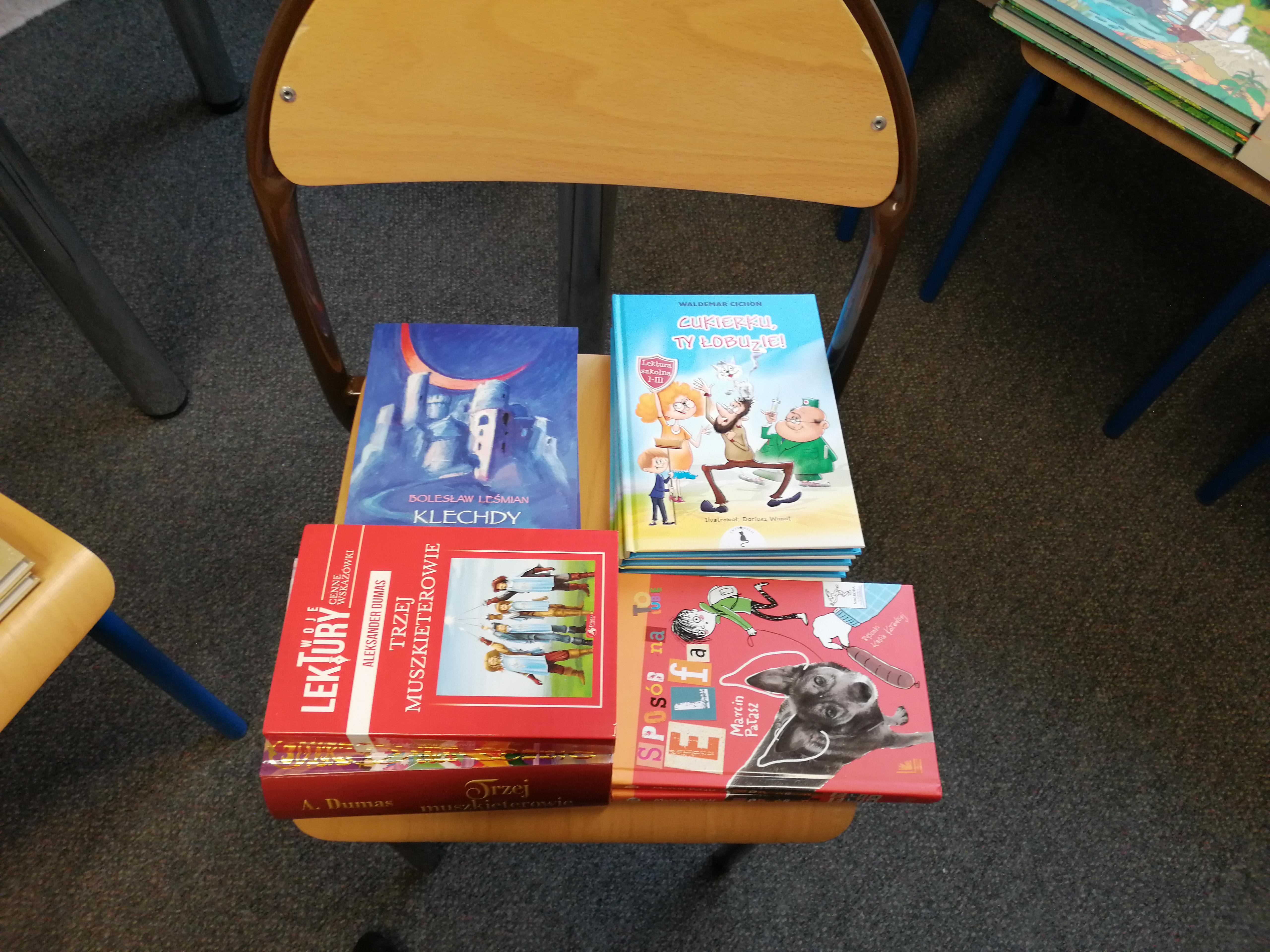 Książki dla uczniów z programu rozwoju czytelnictwa rozłożone na krzesełku szkolnym