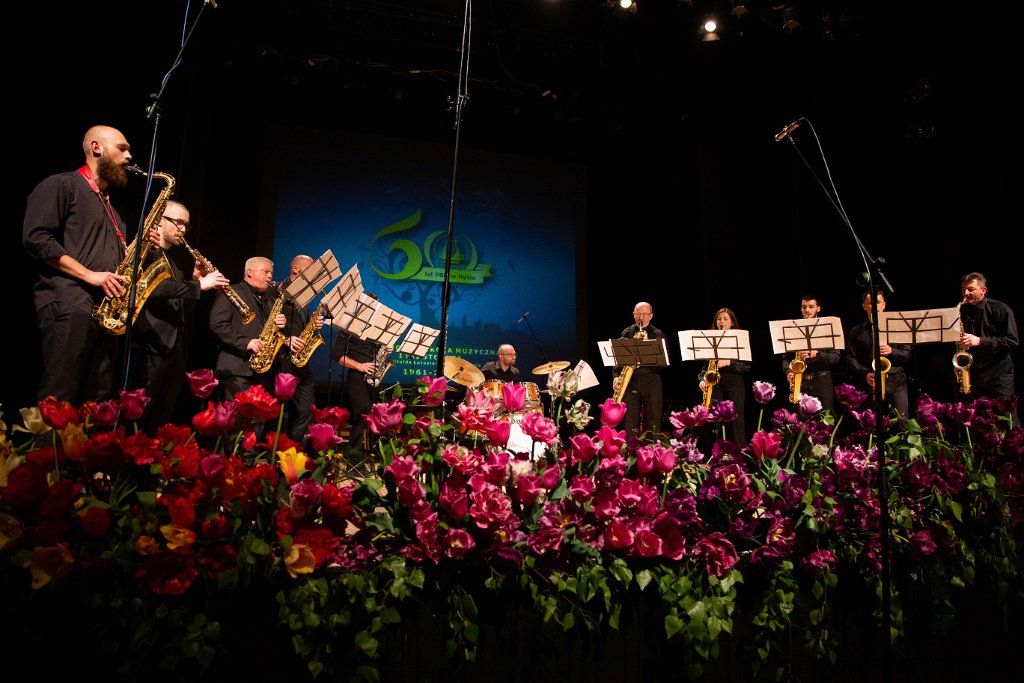 Zdjęcie. Jubileusz 60-lecia PSM w Nysie - II Koncert Jubileuszowy - 14 maja 2022 - Nyski Dom Kultury. Na scenie w trakcie występu zespół saksofonistów. Z przodu bukiety kwiatów. W tle baner z logo szkoły i perkusista. Kliknięcie na zdjęcie przeniesie do prezentacji cyklu zdjęć z koncertu.