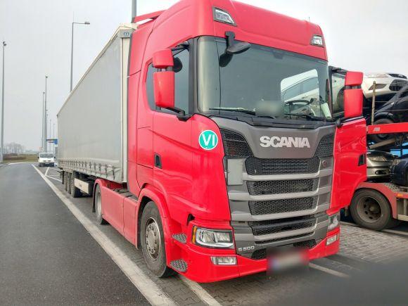 Na pierwszym planie czerwony ciągnik samochodowy wraz z naczepą