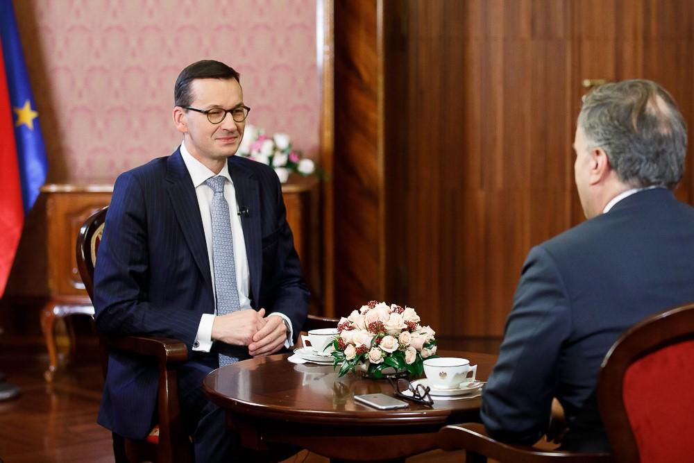 Premier Mateusz Morawiecki siedzi przy stole podczas udzielania wywiadu, przed nim dziennikarz.