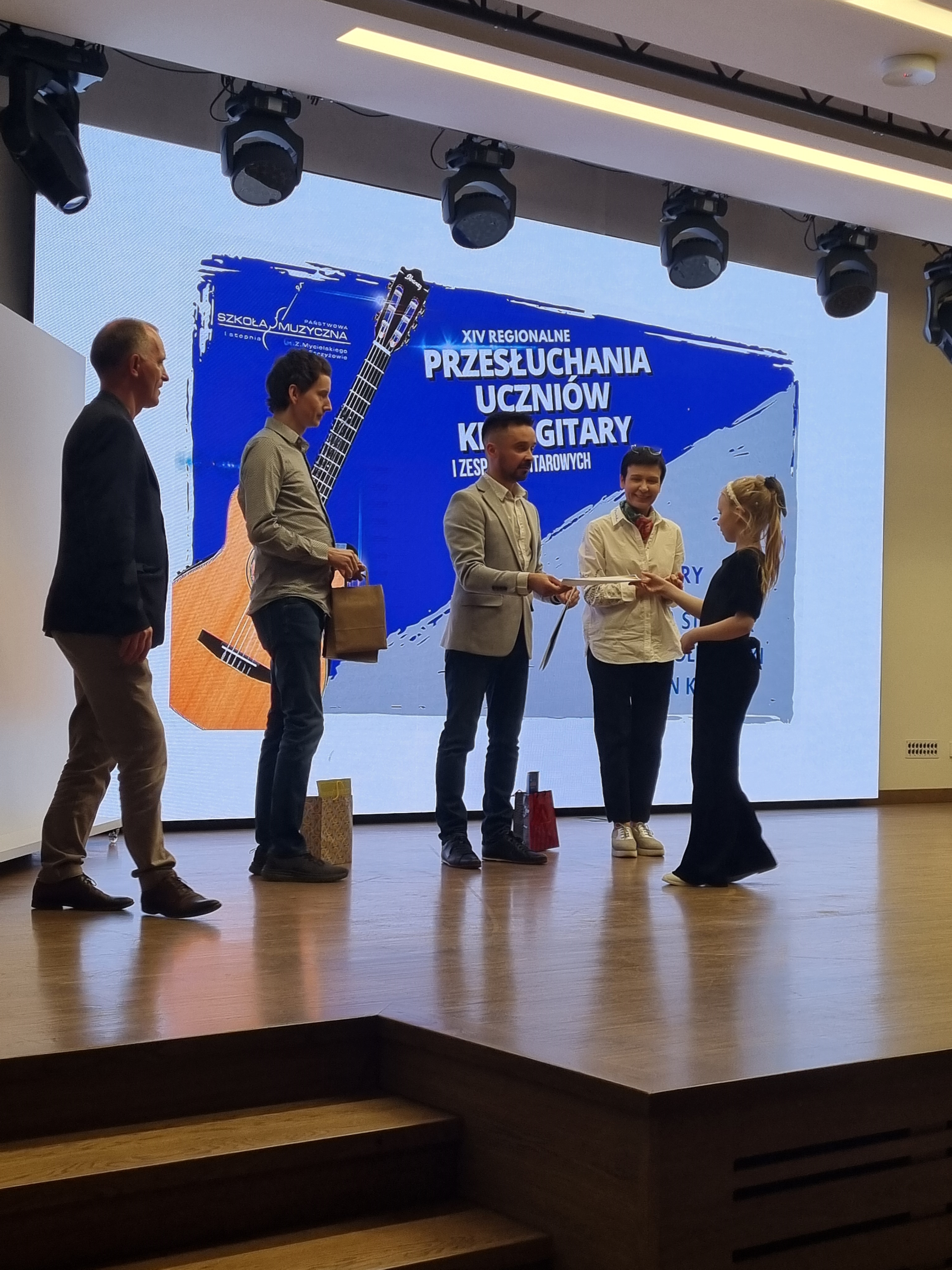 Zdjęcie przedstawiające przedstawicieli Jury wręczających na scenie dyplom