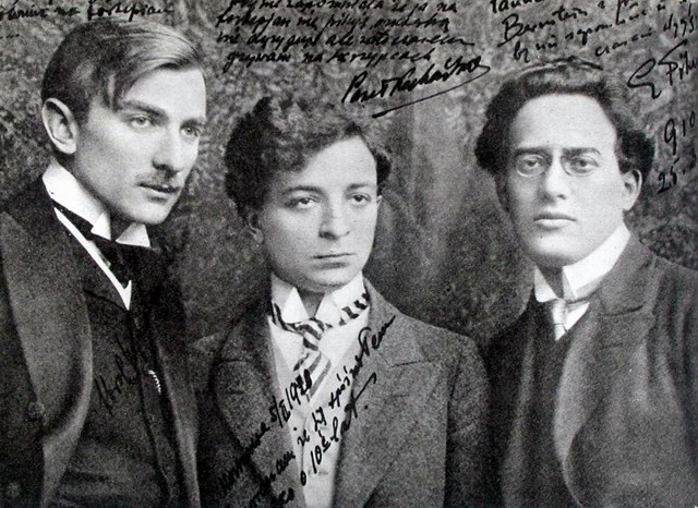 Czarno-biała fotografia trzech mężczyzn, pozujących do zdjęcia. Od lewej-Karol Szymanowski, Paweł Kochański, Grzegorz Fitelberg. Zdjęcie z 1910 roku. Na zdjęciu nieco nieczytelne, odręczne notatki.