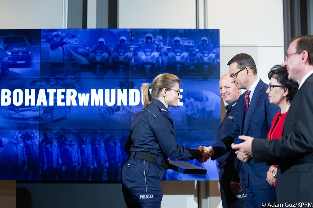 Uścisk dłoni funkcjnariuszki i premiera Morawieckiego, a w tle napis "Bohater w mundurze".