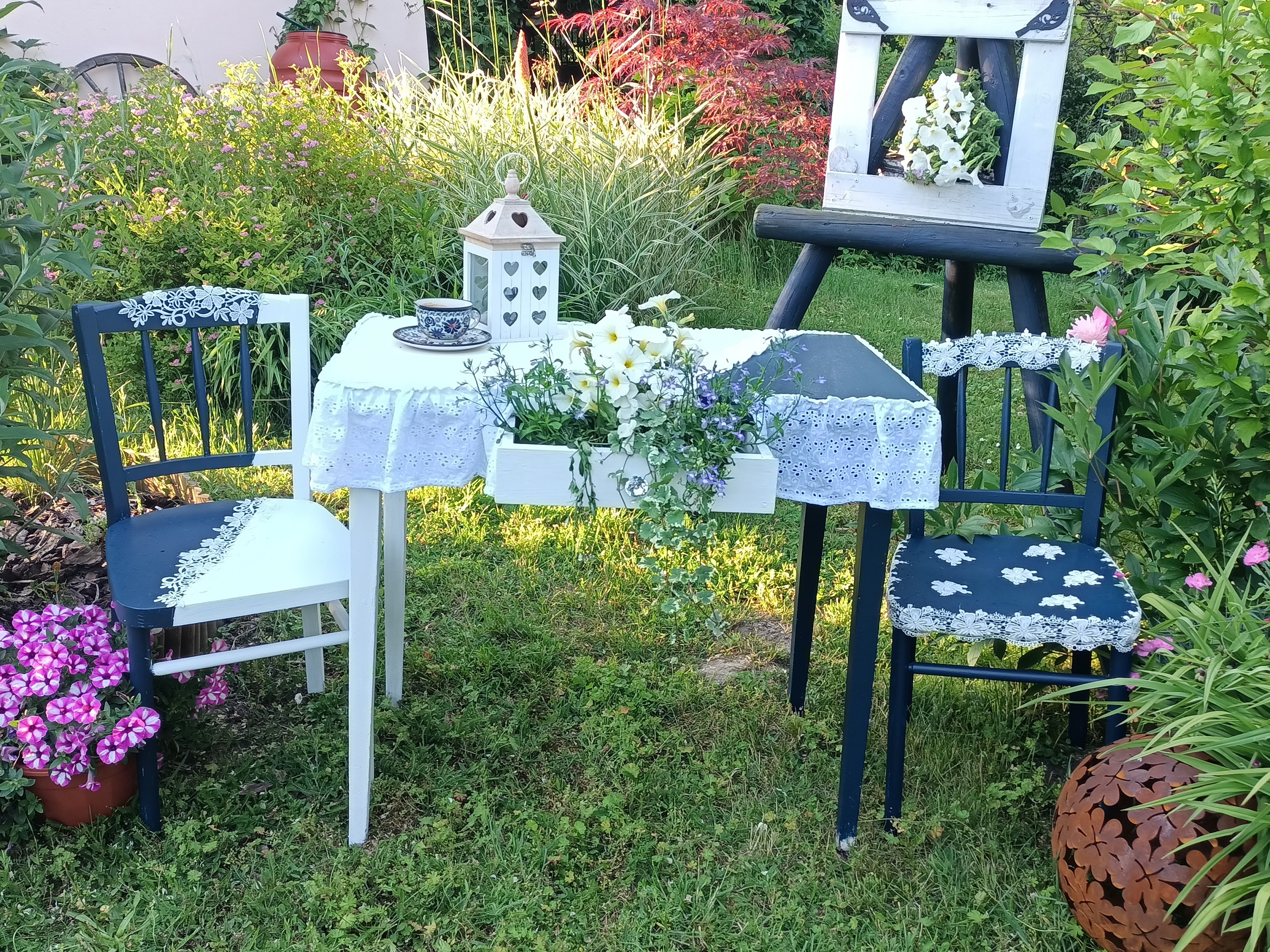 dwa biało-granatowe krzesła i stolik przykryty obrusem, stojące w ogrodzie