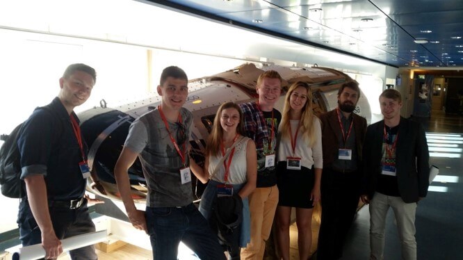 Grupa studentów na tle białej, podłużnej maszyny