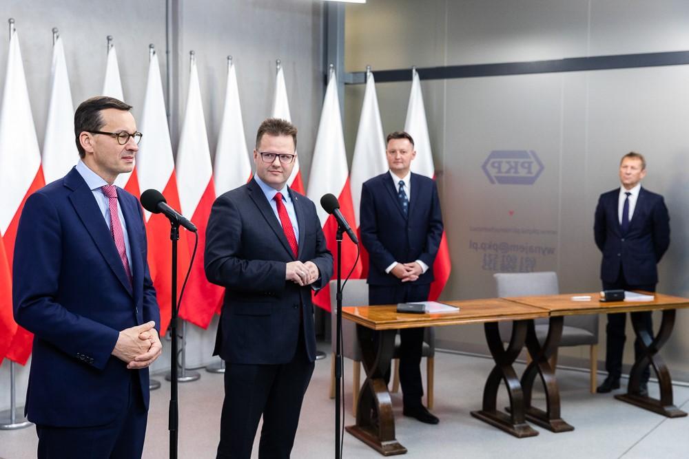 Premier Mateusz Morawiecki i wiceminister Andrzej Bittel stoją przy mikrofonach.