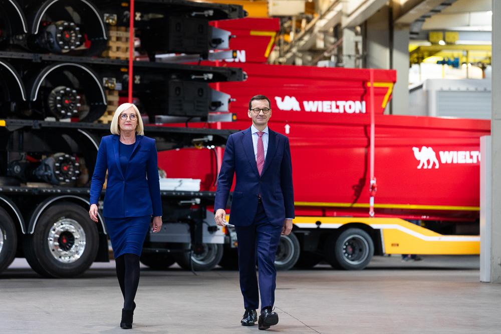 Premier Mateusz Morawiecki i minister Joanna Kopcińska idą na tle przyczep firmy Wielton.