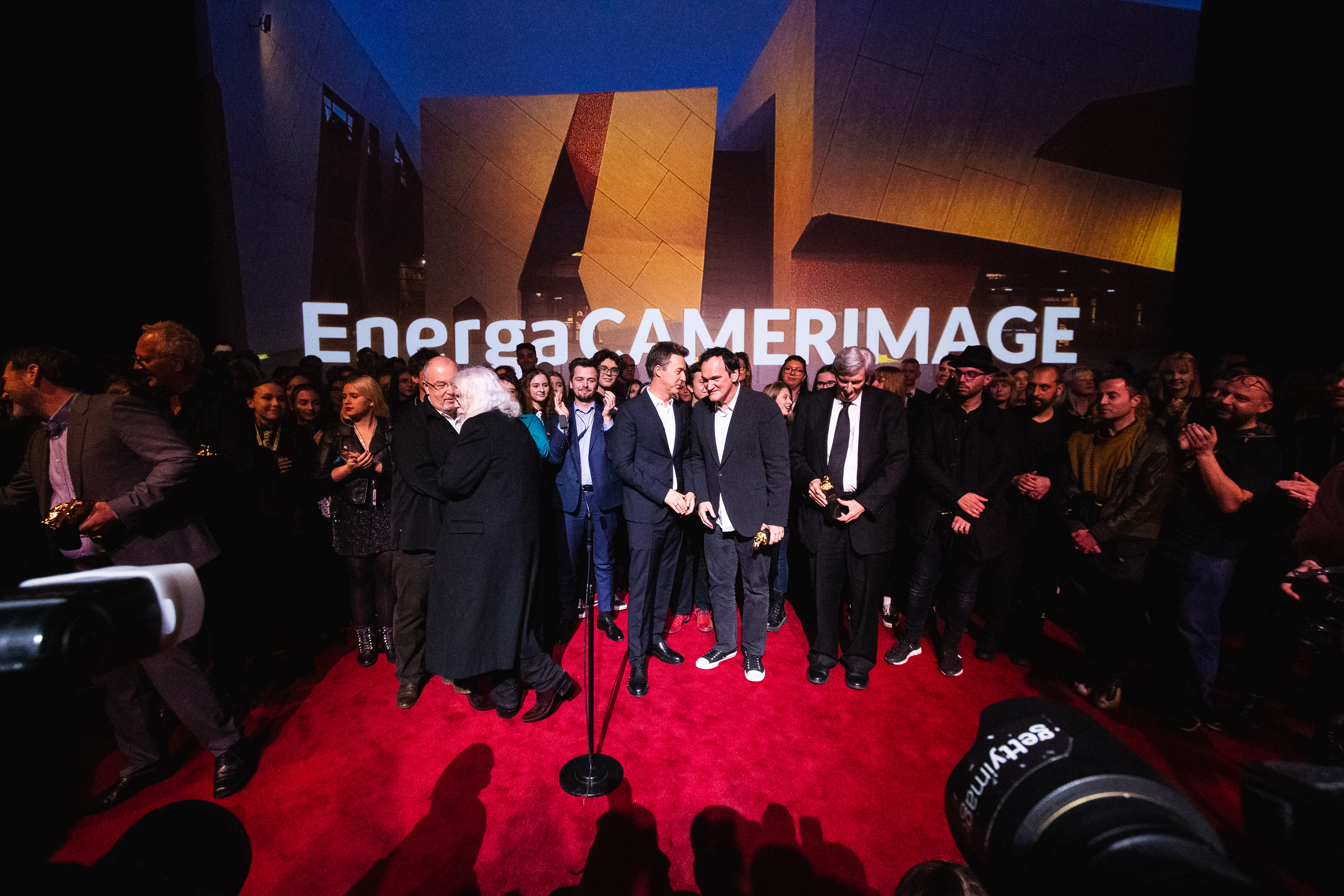 Gala zamknięcia wydarzenia. Na czerwonym dywanie tłum znakomitości, wśród nich reżyser Quentin Tarantino. Na podłodze cienie fotoreporterów, na pierwszym planie widoczny fragment obiektywu