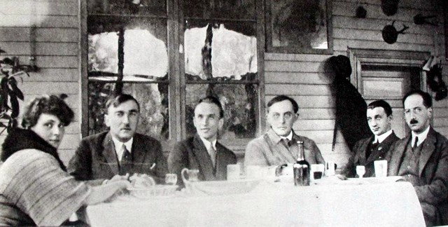 Czarno-białe zdjęcie grupy osób siedzących przy stole na werandzie drewnianego domu. Od lewej: A. Iwaszkiewicz, K. Szymanowski, J. Iwaszkiewicz, S. I. Witkiewicz, S. Mierczyński, J. Mieczysławski.