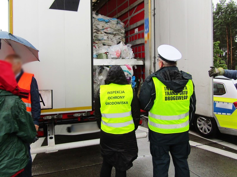 Funkcjonariusze Inspekcji Transportu Drogowego i Inspekcji Ochrony Środowiska w trakcie kontroli. Na zdjęciu dwóch inspektorów stoi przed ciężarówką, którą przewożono odpady i zaglądają do naczepy.