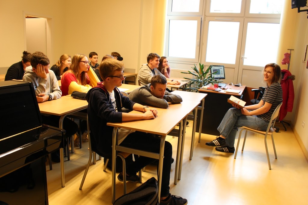 Grafika przedstawi uczniów zgtomadzonych w klasie, słuchających głośnego czytania