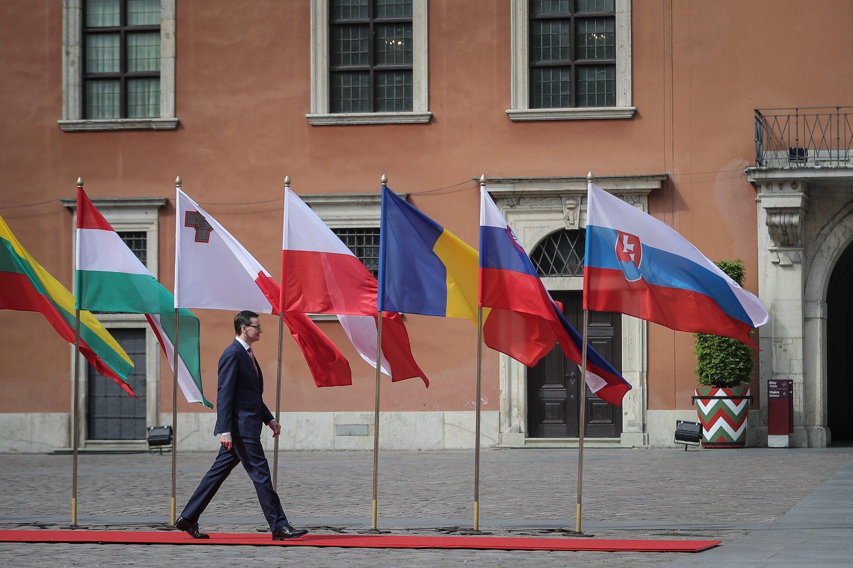 Premier Mateusz Morawiecki, a w tle powiewające flagi.