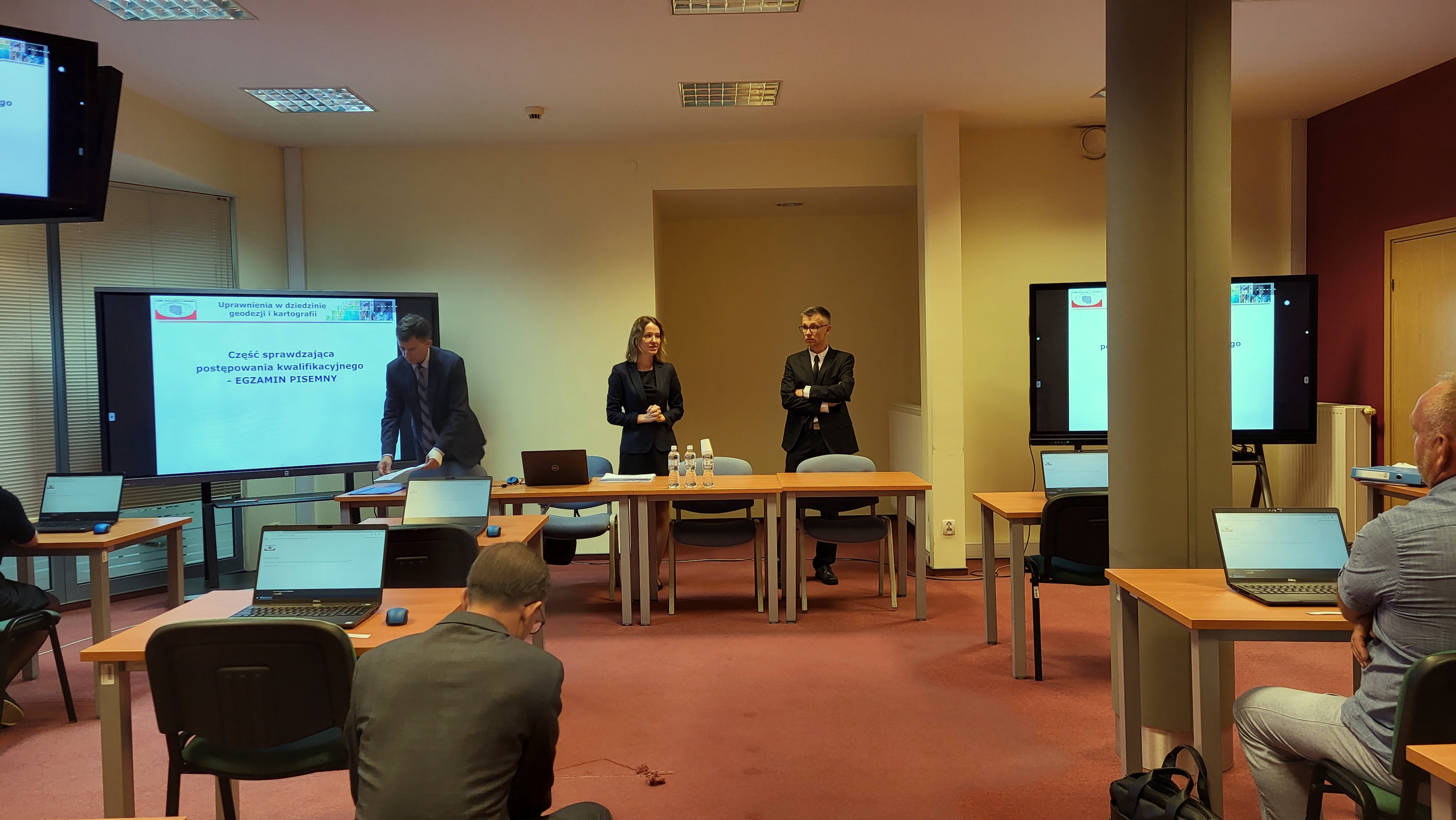 Zdjęcie przedstawia salę egzaminacyjną z członkami Komisji egzaminacyjnej i osobami przystępującymi do egzaminu siedzącymi pojedynczo przed laptopami