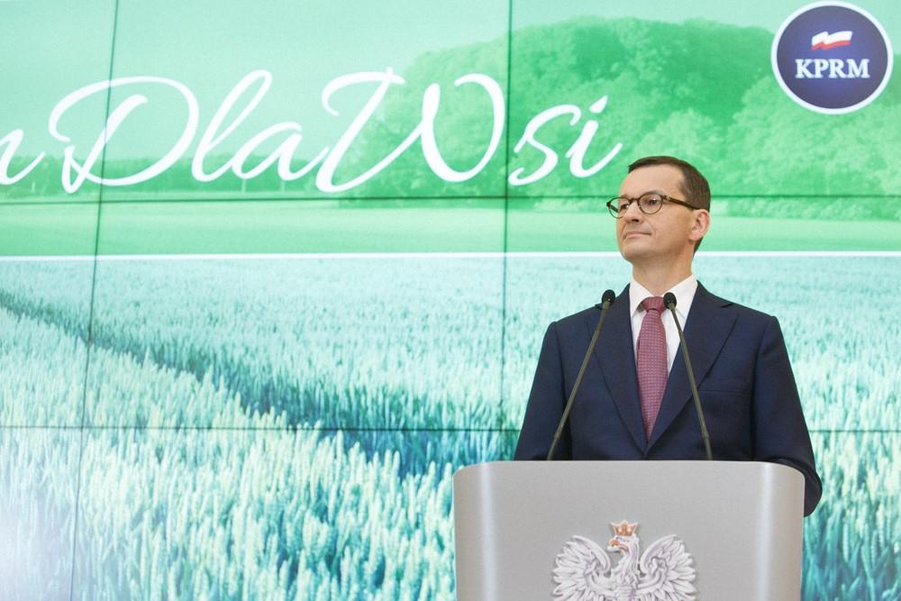 Premier Mateusz Morawiecki przy mównicy, a w tle prezentacja #PlanDlaWsi.