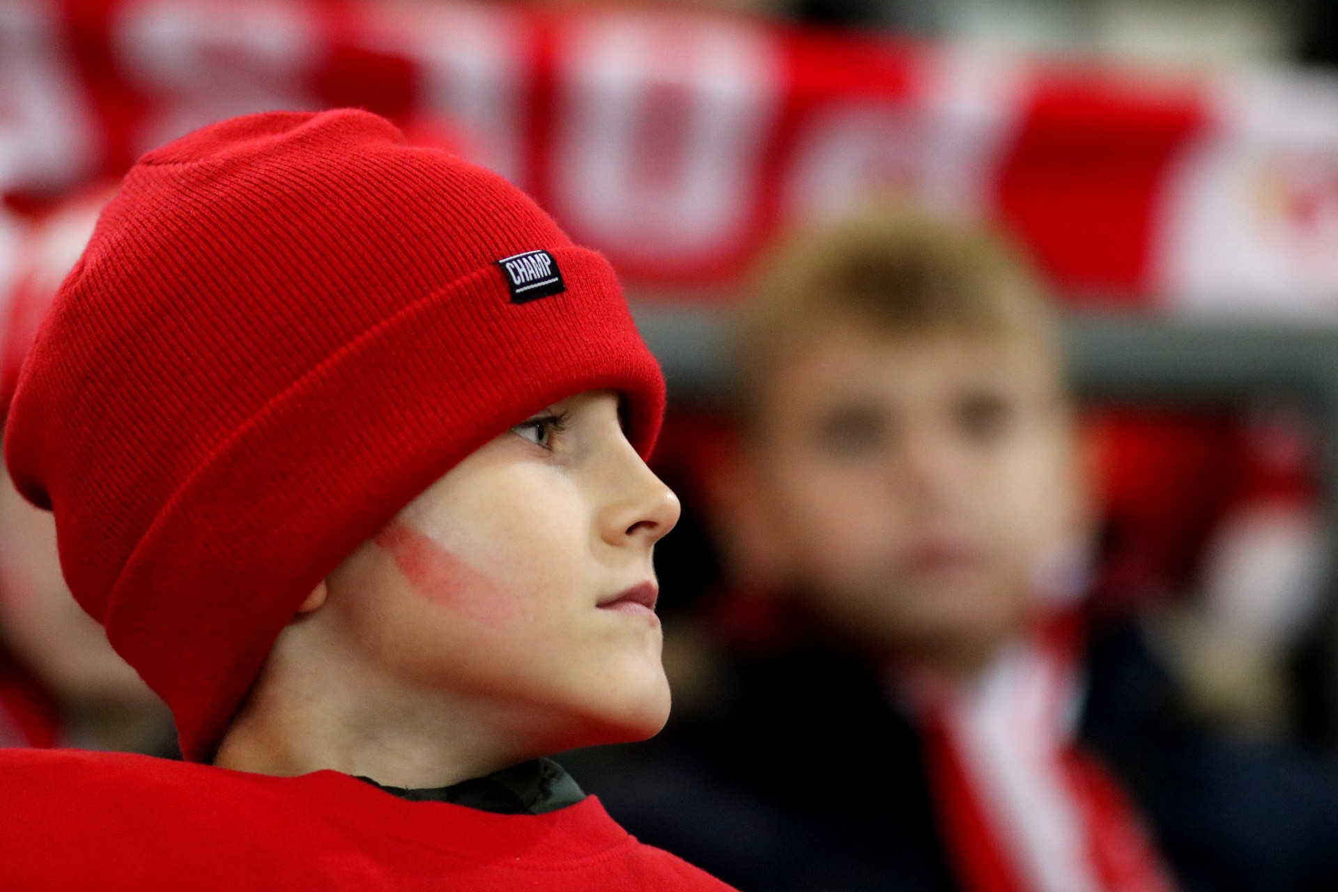 Twarz chłopca w czerwonej czapce i z namalowanymi na policzkach biało-czerwonymi paskami.