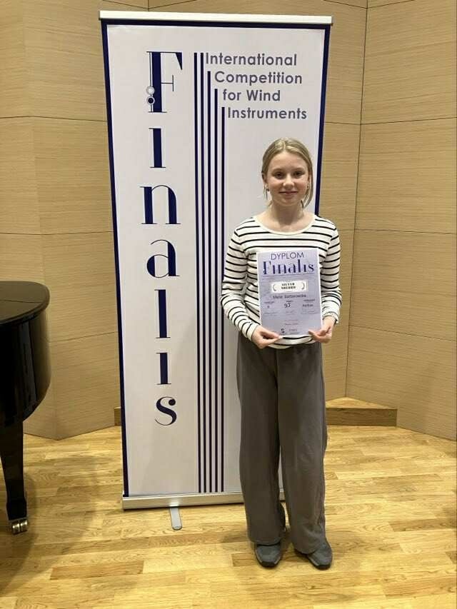 Uczennica stoi przed ścianką reklamową konkursu i trzyma dyplom. 