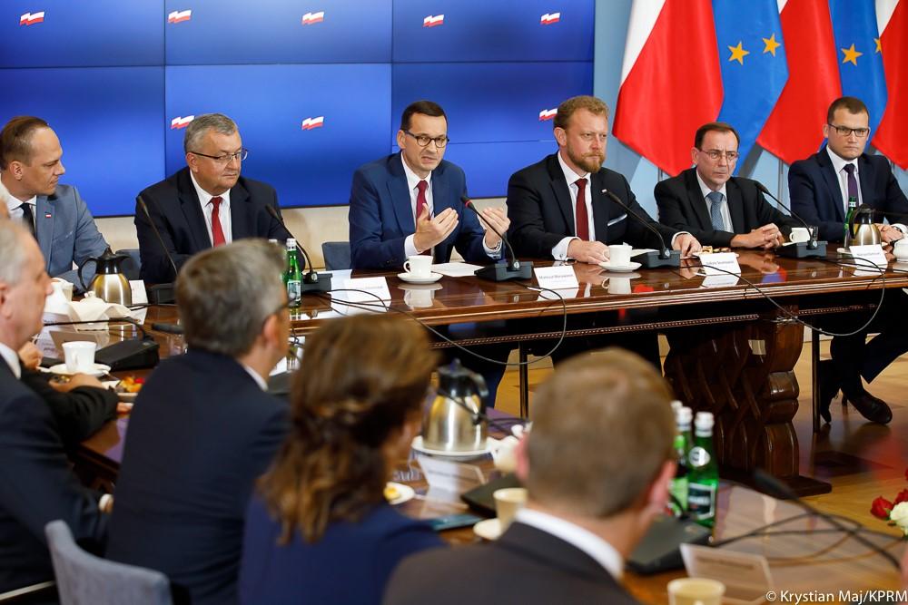 Premier Mateusz Morawiecki mówi do siedzących przy stole wojewodów, a obok niego siedzą ministrowie. 