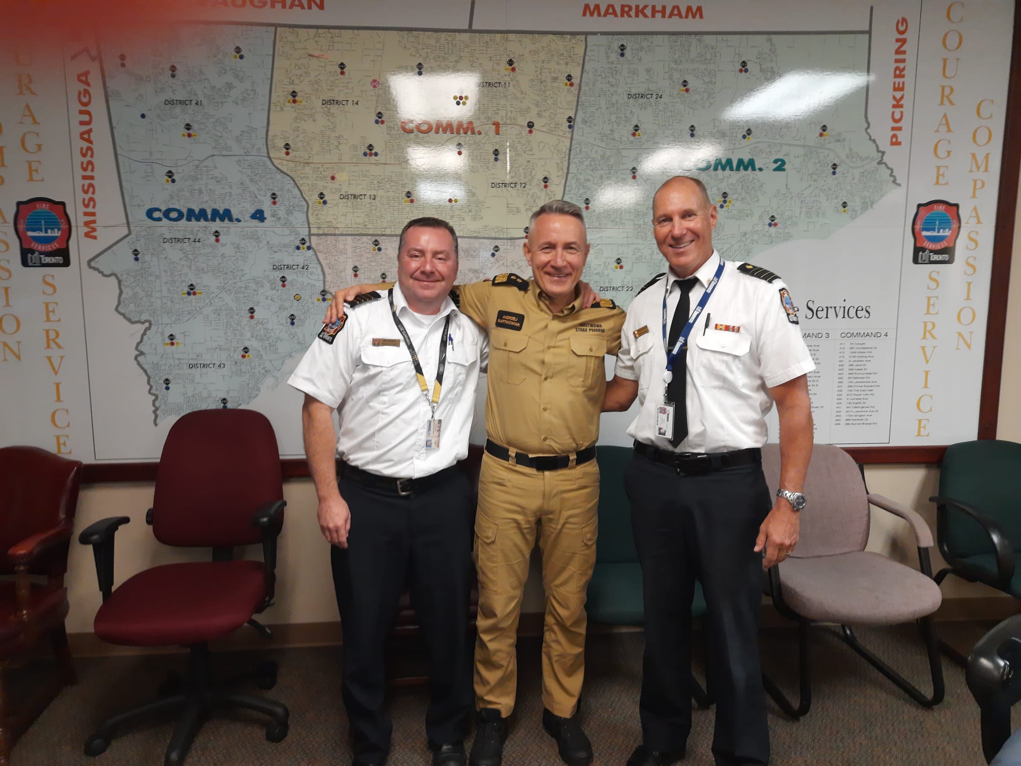 Komendant główny PSP stoi wspólnie z dwoma kanadyjskimi strażakami - za nimi mapa terenu