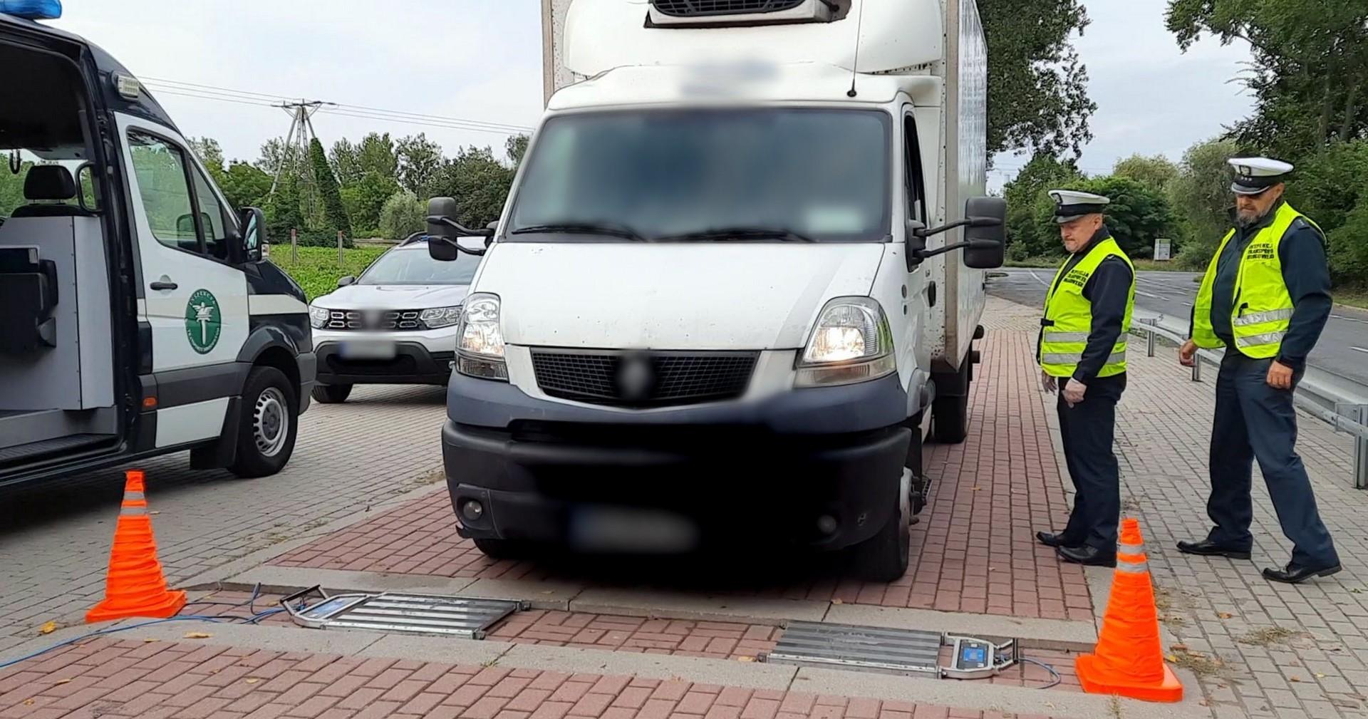Bus wjeżdża na wagi ITD. Obok stoją inspektorzy i radiowóz ITD.
