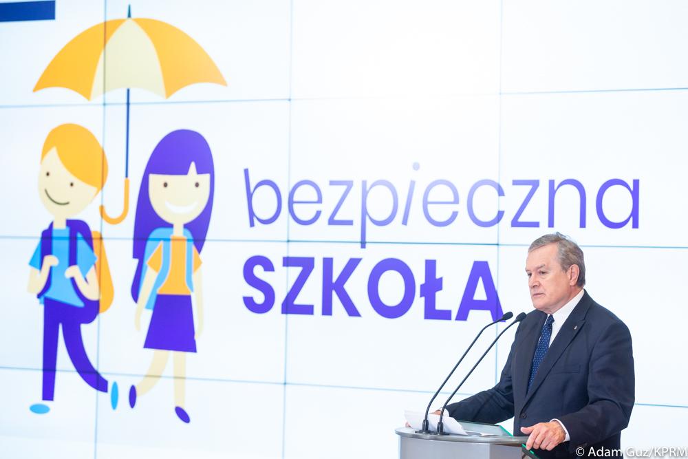 Wicepremier Piotr Gliński przemawia na tle ścianki wizyjnej.