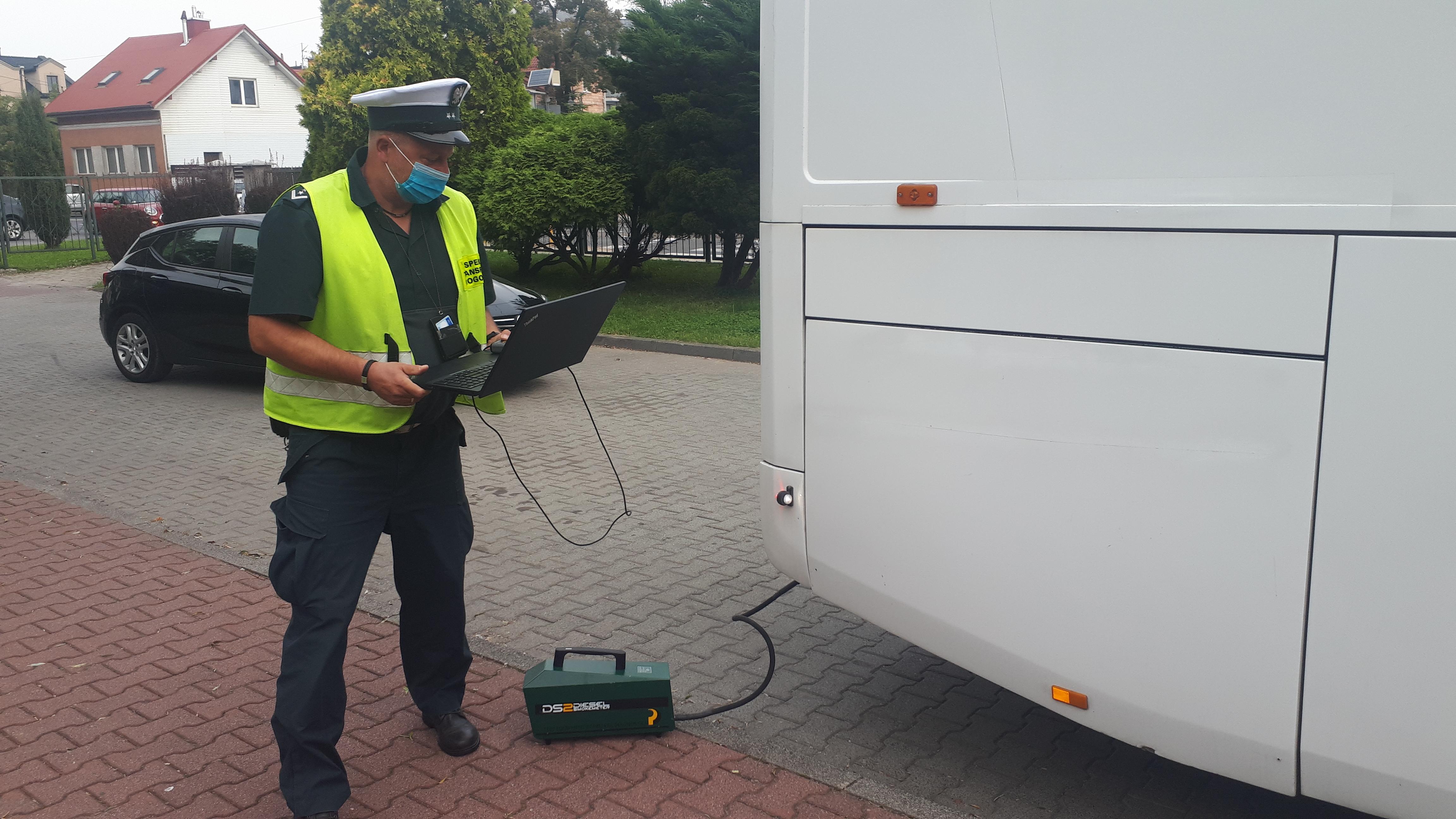 Inspektor z laptopem obok dymomierza podłączonego do rury wydechowej autobusu