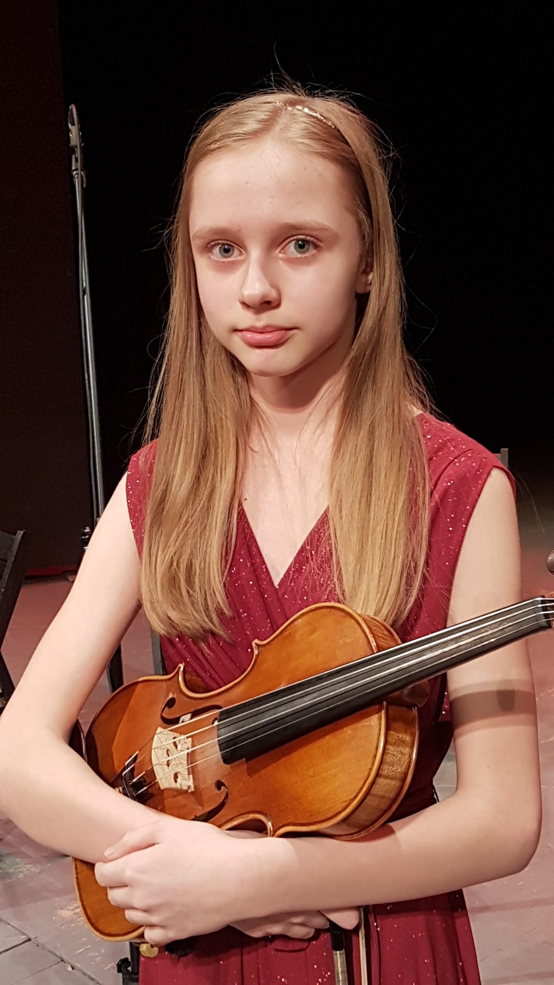 Zdjęcie uczennicy Aleksandry Urban. Uczennica trzyma skrzypce, ubrana w czerwoną sukienkę.