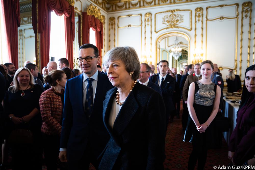 Premier Mateusz Morawiecki i premier Theresa May idą, a za nimi podąża grupa osób.