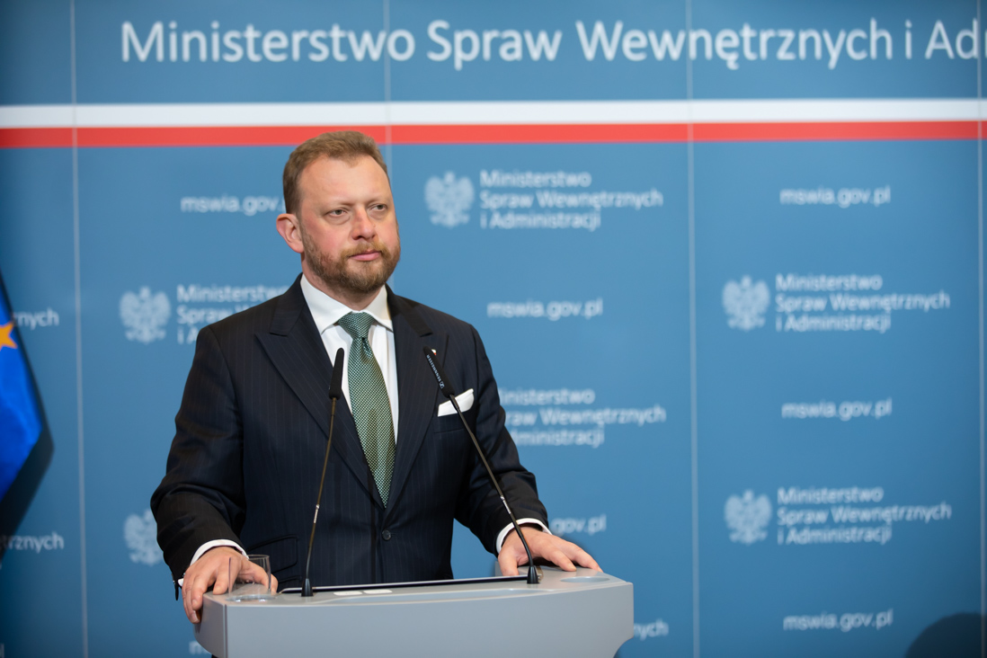 Na zdjęciu widać ministra Łukasza Szumowskiego stojącego na tle ścianki MSWiA podczas konferencji prasowej.