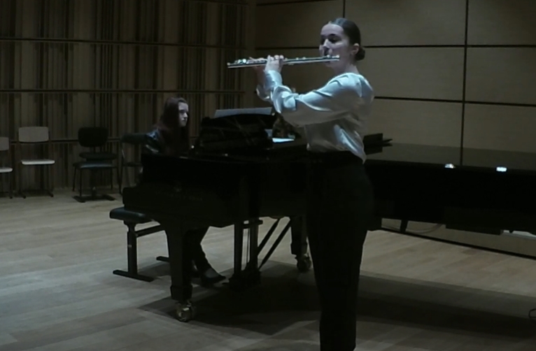 Uczennica grająca na flecie z towarzyszeniem nauczyciela na fortepianie.