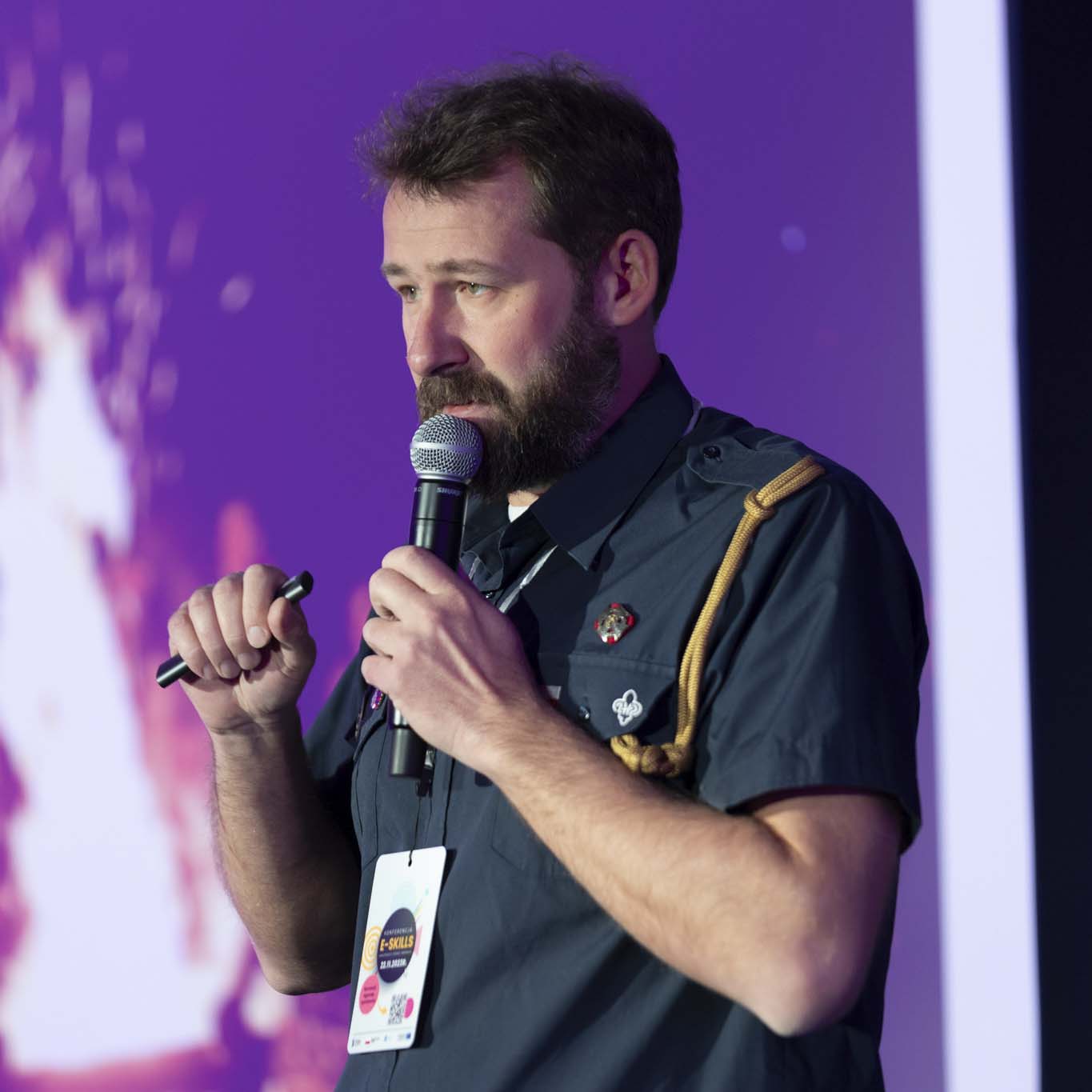 Pan Tomasz Rejmer, instruktor harcerski w stopniu harcmistrza trzyma mikrofon w ręku. Przemawia.