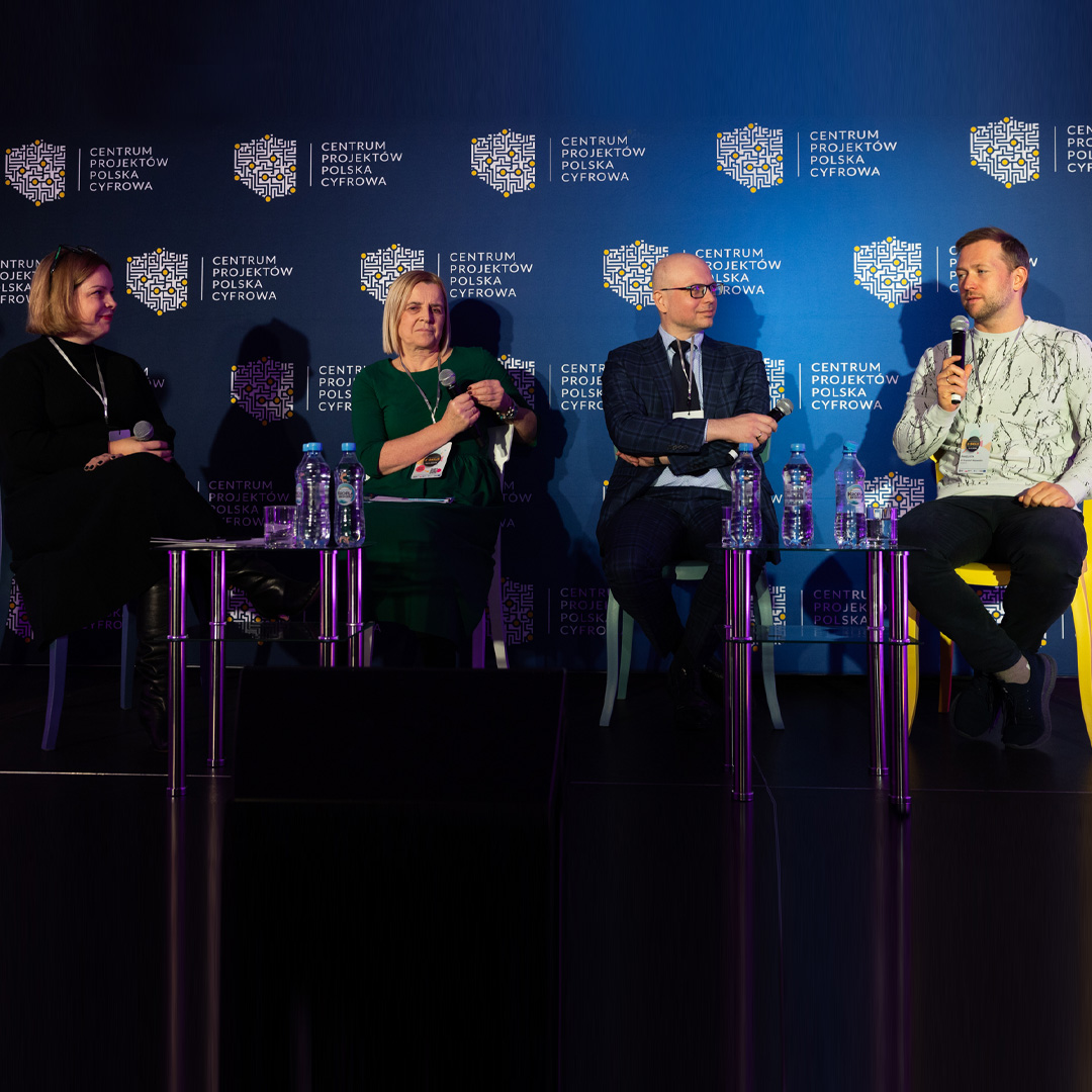Czwórka panelistów siedzi na krzesłach na podium. Doktor Krzysztof Wojewodzic mówi do mikrofonu, reszta uczestników słucha wypowiedzi.