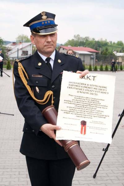 Komendant Miejski PSP trzyma w ręku i prezentuje Akt oddania strażnicy. W ręce trzyma tez tubę do przechowywania aktu.