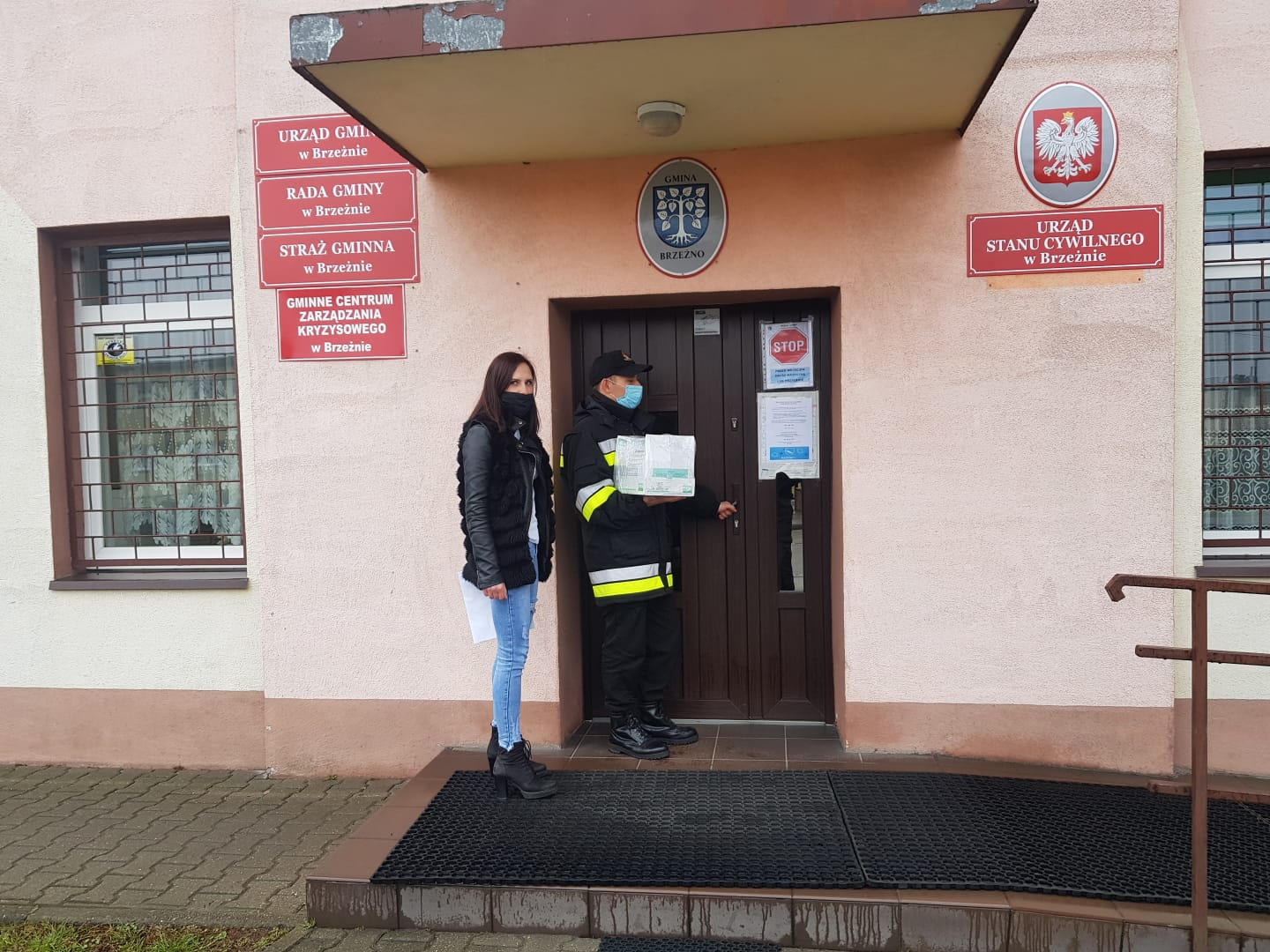 Zdjęcie przedstawia strażaka oraz młodą kobietę, którzy wchodzą do siedziby gminy Brzeżno z kartonem ulotek #szepimysię