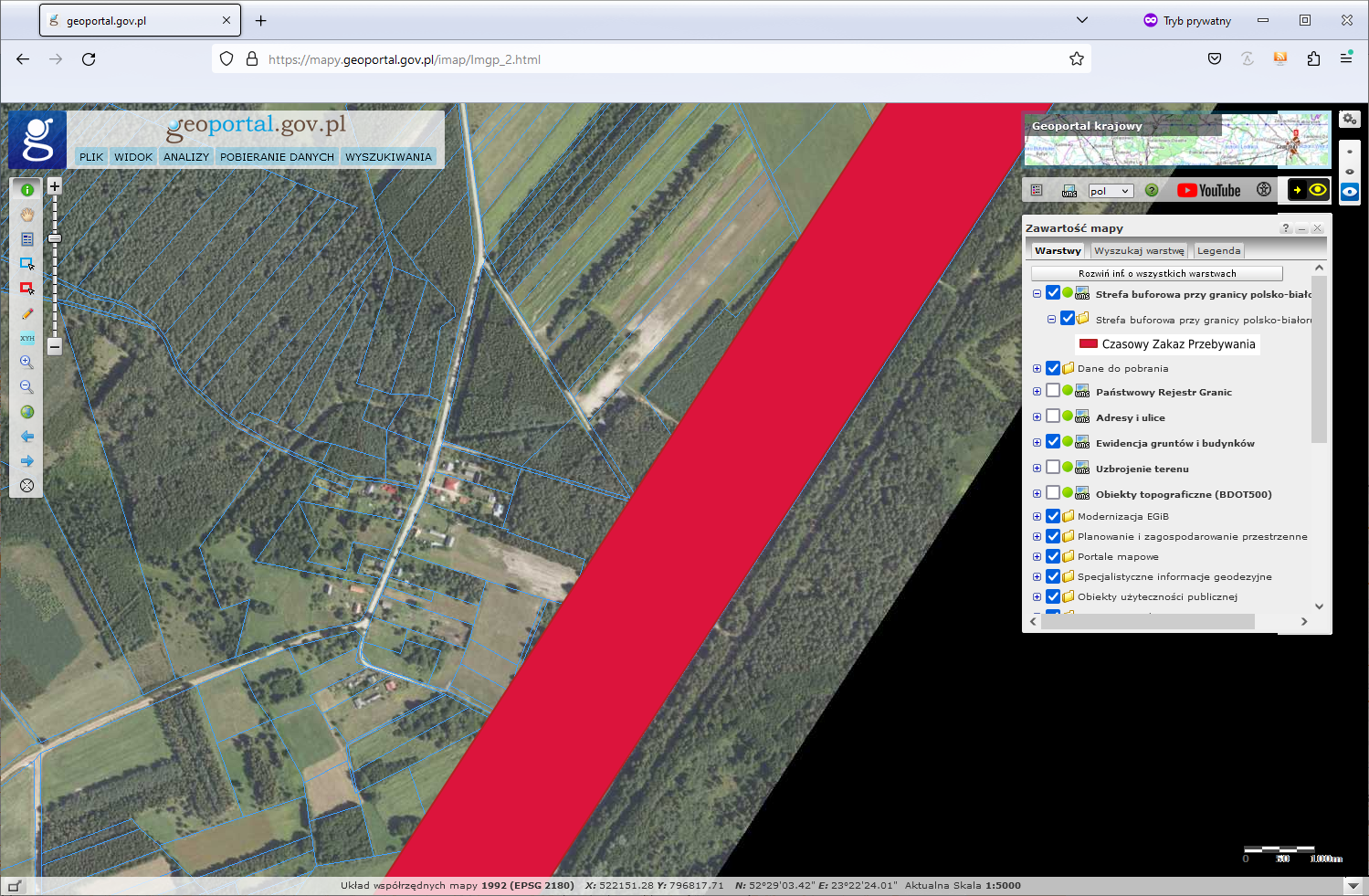 Ilustracja przedstawia przebieg warstwy Strefa buforowa przy granicy polsko-białoruskiej w serwisie geoportal.gov.pl w pobliżu zabudowań.