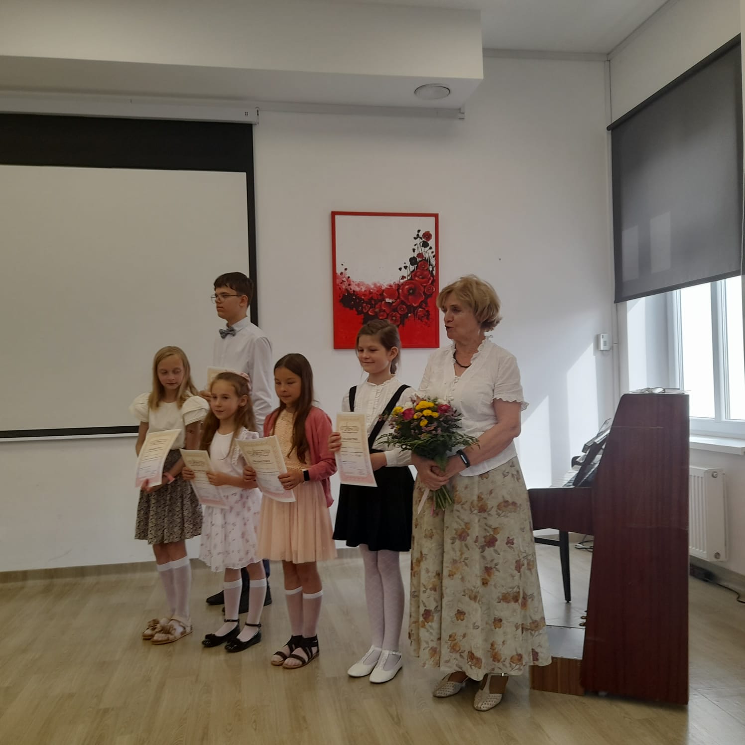 Grupa pięciu uczniów trzymająca dyplomy wraz z nauczycielem p. Martą Dąbrowską stoją na tle fortepianu