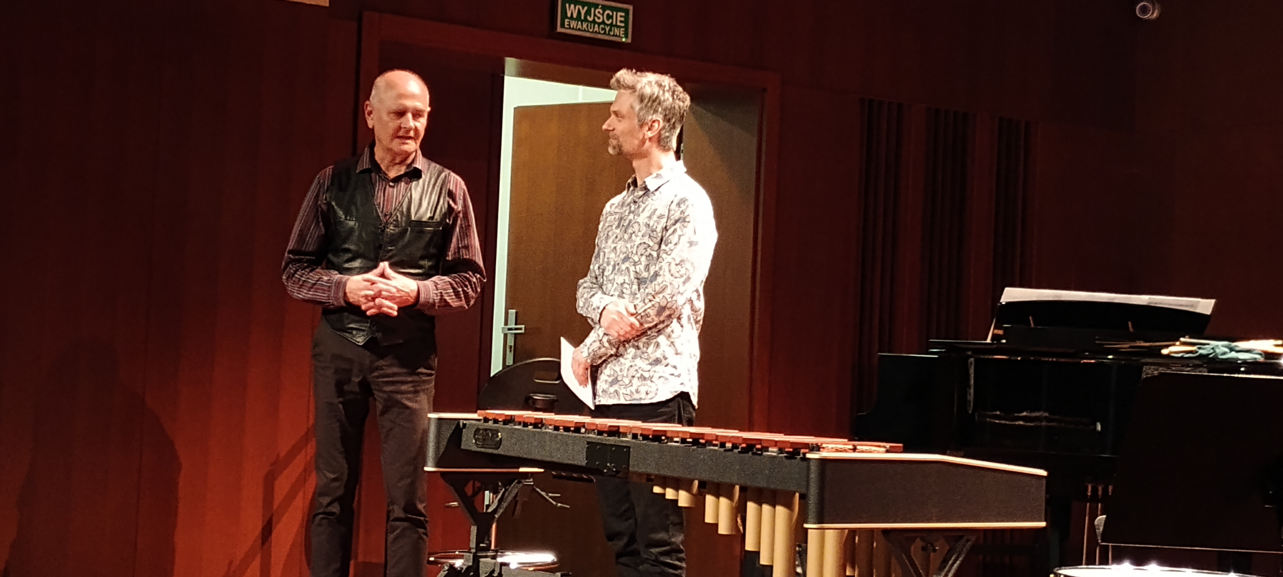 Warsztaty perkusyjne w szkole. Dyrektor szkoły i prowadzący warsztaty na scenie sali koncertowej.