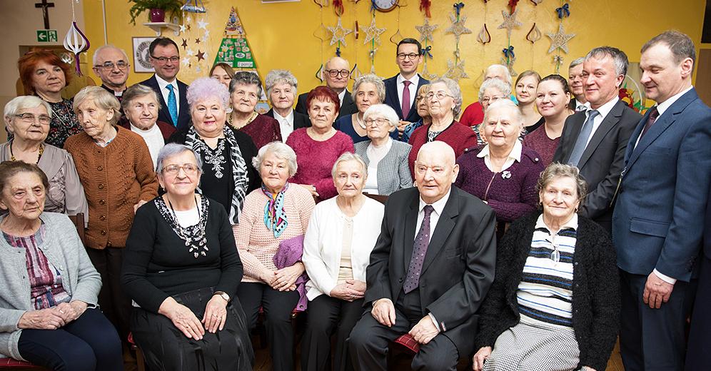 Premier Mateusz Morawiecki pozuje do zdjęcia z seniorami.