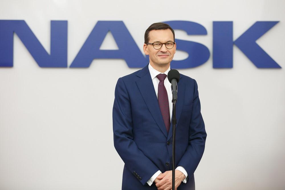 Premier Mateusz Morawiecki stoi na tle napisu NASK.