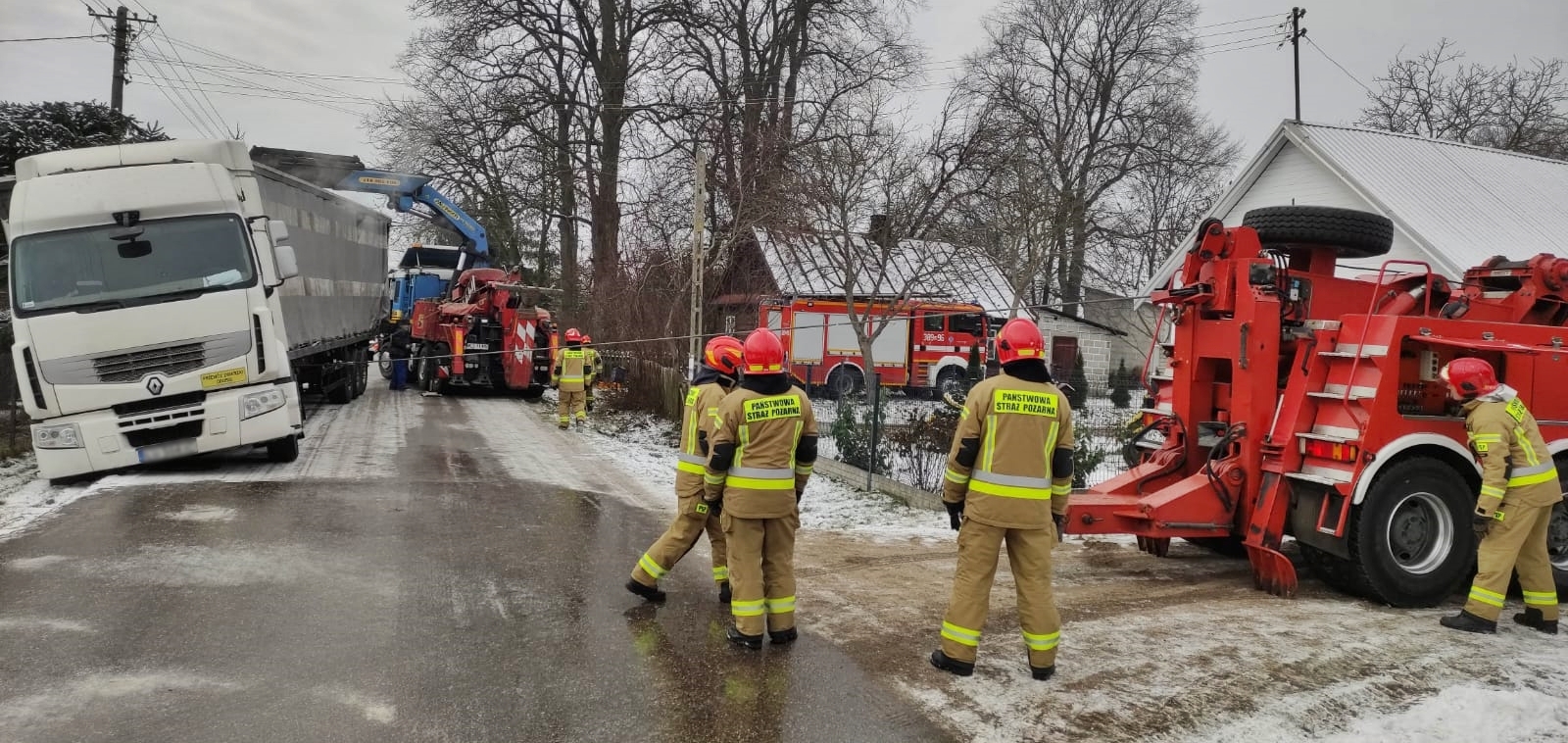 Na zdjęciu przechylony samochód ciężarowy, który zsunął się z drogi na pobocze. Strażacy z pomocą wyciągarek samochodowych stabilizując pojazd.