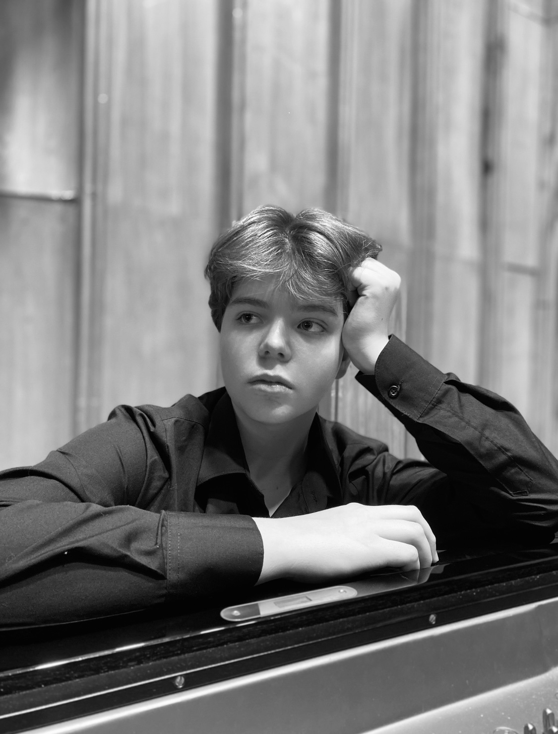 Zdjęcie czarno-białe chłopaka w czarnej koszuli opartego o fortepian.