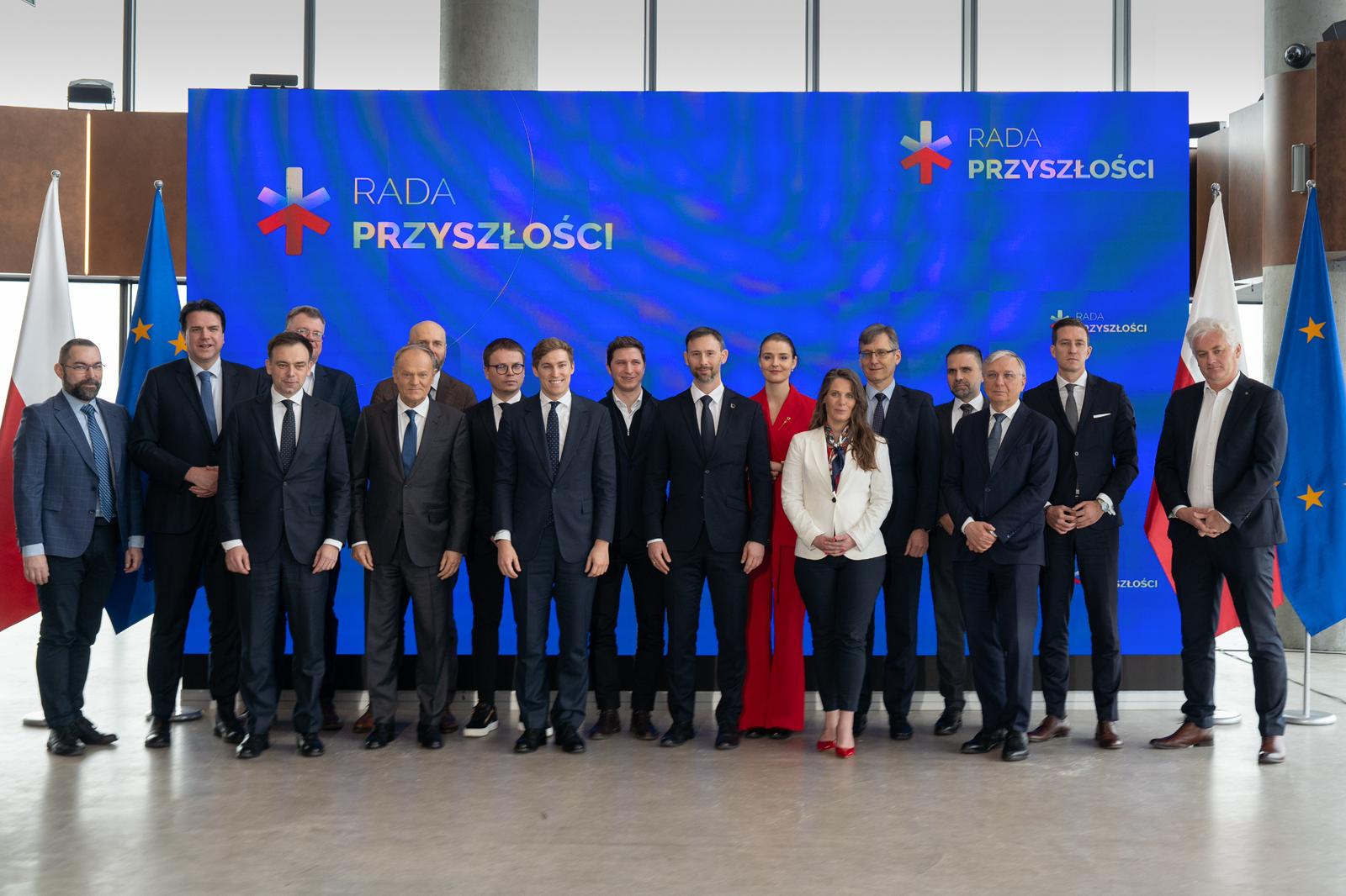 Na tle niebieskiego banera z logo Rady Przyszłości i napisem Rada Przyszłości widać 17 osób wchodzących w skład Rady, w tym Premier Donald Tusk i Minister Finansów i Gospodarki Andrzej Domański