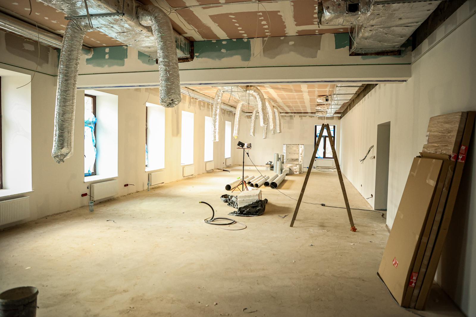 Wnętrze pomieszczenia w trakcie remontu, na podłodze leżą rury, o ścianę oparte są płyty