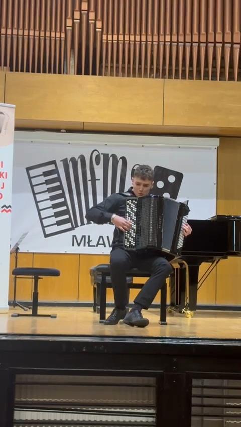 Zdjęcie - Mateusz Neckar w trakcie konkursu akordeonowego w Mławie. Uczeń w trakcie wykonywania utworu na akordeonie na scenie konkursu