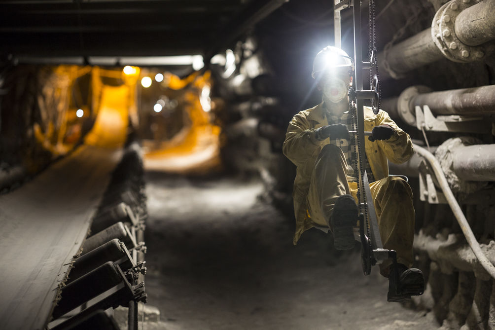 Szyb kopalniany. Na pierwszym planie mężczyzna przemieszczający się na monobiku. Ubrany jest w żółty strój roboczy. Włączoną ma latarkę na kasku