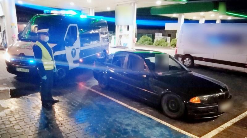 Oznakowany radiowóz ITD stoi za zatrzymanym do kontroli na terenie stacji benzynowej samochodem osobowym. Obok samochodu osobowego stoi inspektor ITD. 