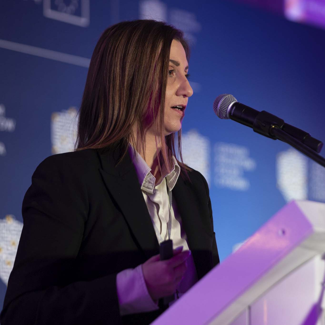 Przy mównicy stoi Pani Maja Wolnik. Wzrok kieruje w stronę uczestników konferencji. Mówi do mikrofonu.