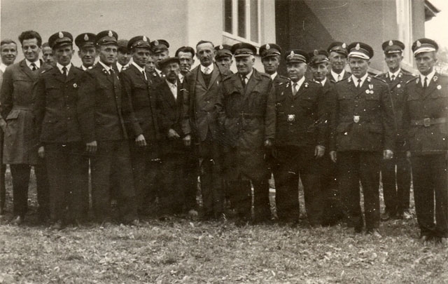 Stanisław Rechowicz - Komendant Powiatowy Straży Pożarnych w Nowym Sączu w latach 1945-1962 stoi w środku z kilkunastoma strażakami w mundurach i czapkach
